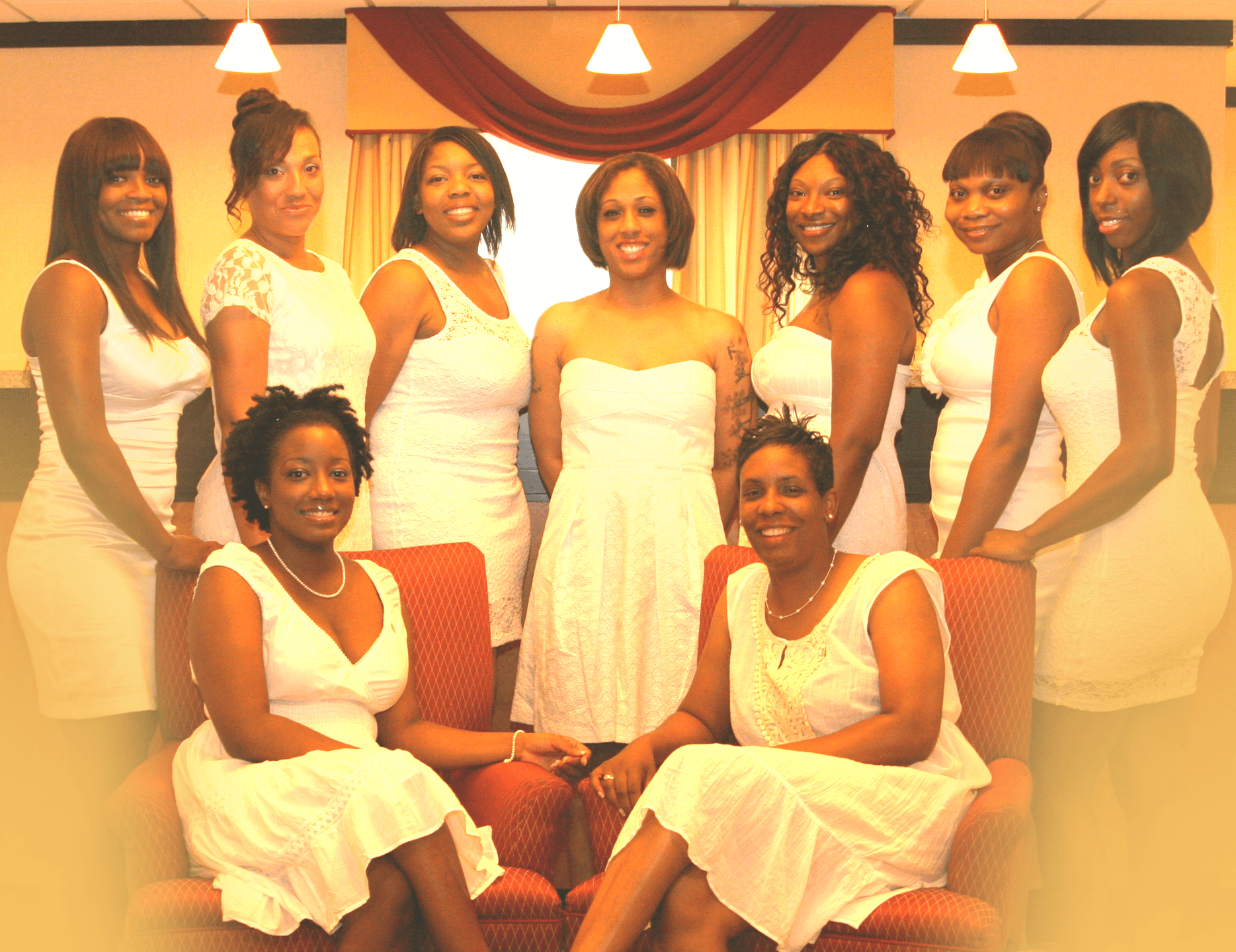 A photo of nine Black women in white dresses, smiling at the camera